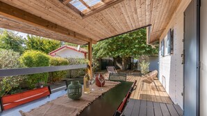 An outdoor patio with a wooden deck, a long table with a bench, and a pergola with a glass ceiling.