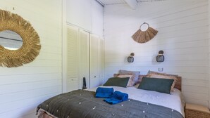 A bedroom with a bed, a round mirror, two wall-mounted speakers, and a woven wall hanging.