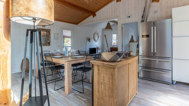 A wooden interior with a dining area, a large lamp, a refrigerator, and a wooden ceiling.