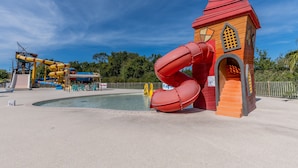 A water park with a red slide and a small building with a flag.