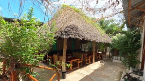 A thatched-roof structure with wooden furniture and a concrete pathway. - Savi House Nungwi (Zanzibar)