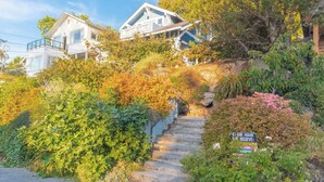 Un edifici residencial amb una escala que condueix a una casa, envoltat de vegetació abundant i un cel clar.