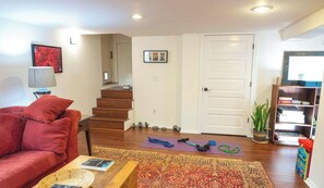 A living room with a red couch, a coffee table with a book, a staircase, a door, and a bookshelf with books.