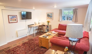 A living room with a sofa, a coffee table, a TV, a desk, and a bookshelf. - Gorgeous 1 Bedroom Space Close to Woodland Park (Seattle)