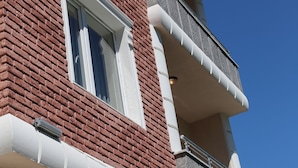 Un edificio de varios pisos con fachada de ladrillo, marcos de ventanas blancos y un balcón con barandilla de metal.