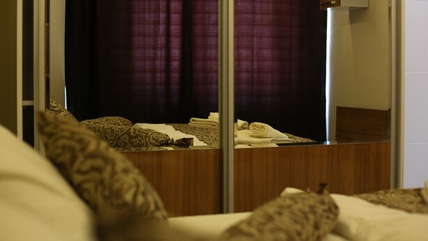Una habitación de hotel con un espejo grande, una cama con almohadones estampados y un cabecero de madera.