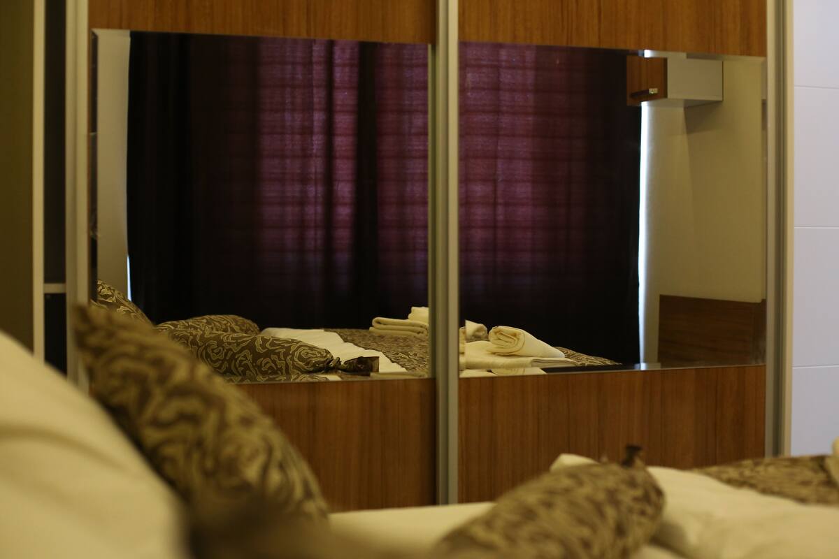 A hotel room with a large mirror, a bed with patterned pillows, and a wooden headboard.