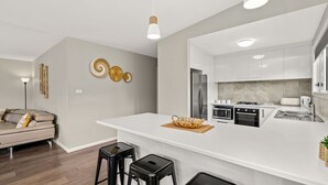 Uma cozinha moderna com armários brancos, eletrodomésticos de aço inoxidável e uma ilha central com banquetas.