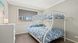 Uma cama beliche com roupa de cama florida em um quarto com janela, escrivaninha e luminária.