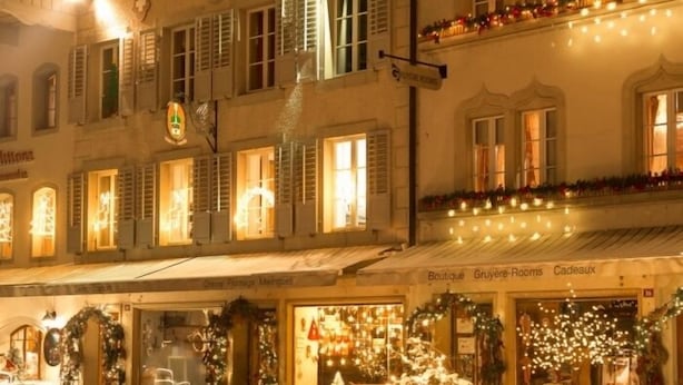 A building with multiple ground-floor shops, including a boutique and a rooming house, decorated with Christmas lights and garlands. - Gruyère-rooms (Gruyeres)