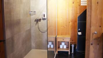 Une salle de bain rustique, avec une cabine de douche en verre, un banc en bois et un sol carrelé de carreaux noirs.