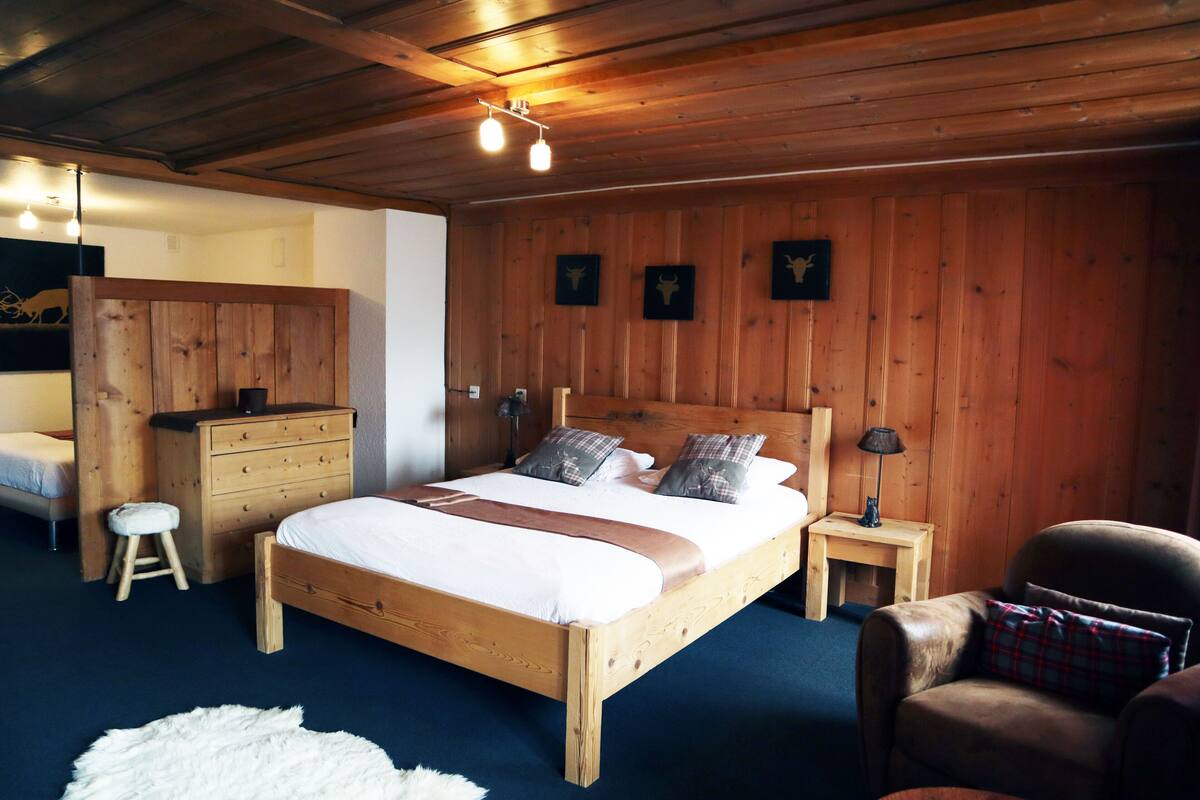 A wooden-paneled bedroom with a bed, dresser, nightstand, chair, and a white furry rug.