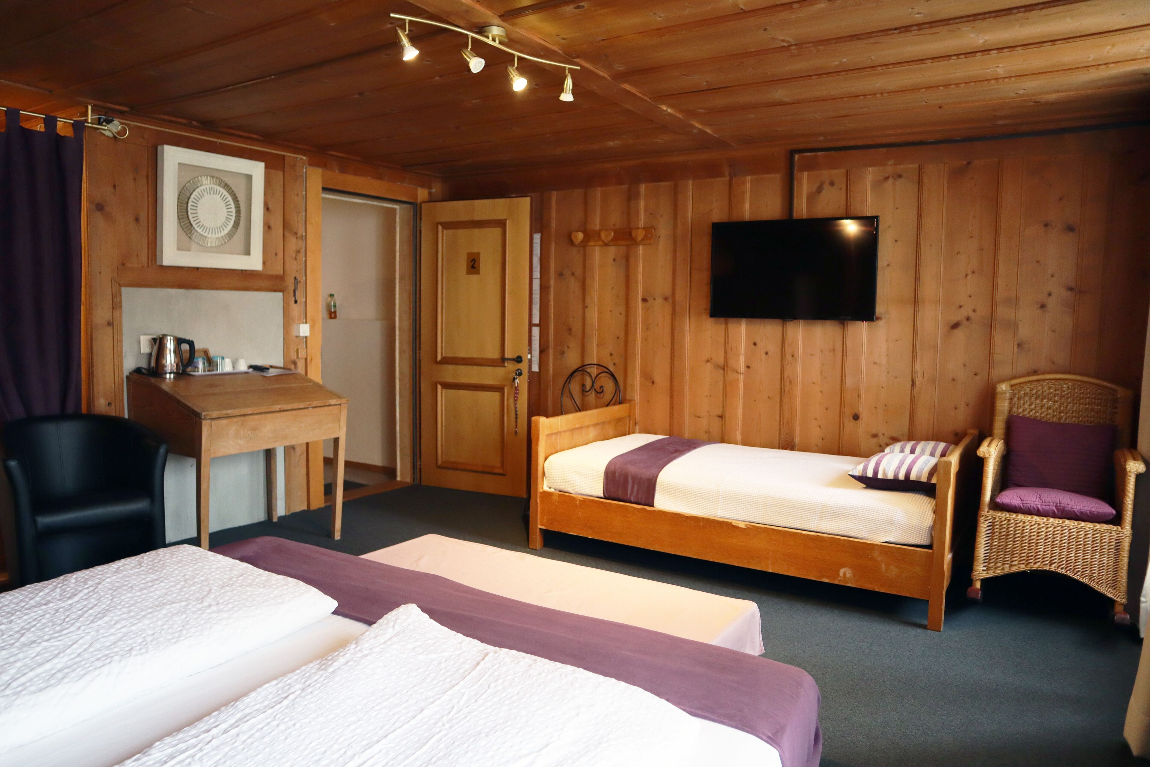 A wooden cabin room with two beds, a desk, a chair, and a TV.