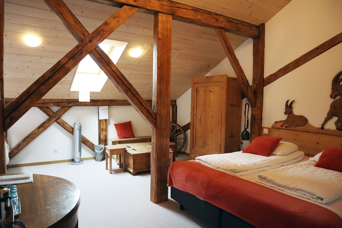 A rustic room with a wooden ceiling, a bed with red bedding, a wooden cabinet, and a wall-mounted heater.