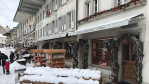 A snow-covered street with shops, including a boutique and a reception area. - Gruyère-rooms (Gruyeres)