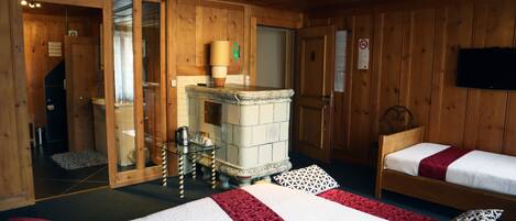 A wooden cabin room with two beds, a fireplace, and a television.