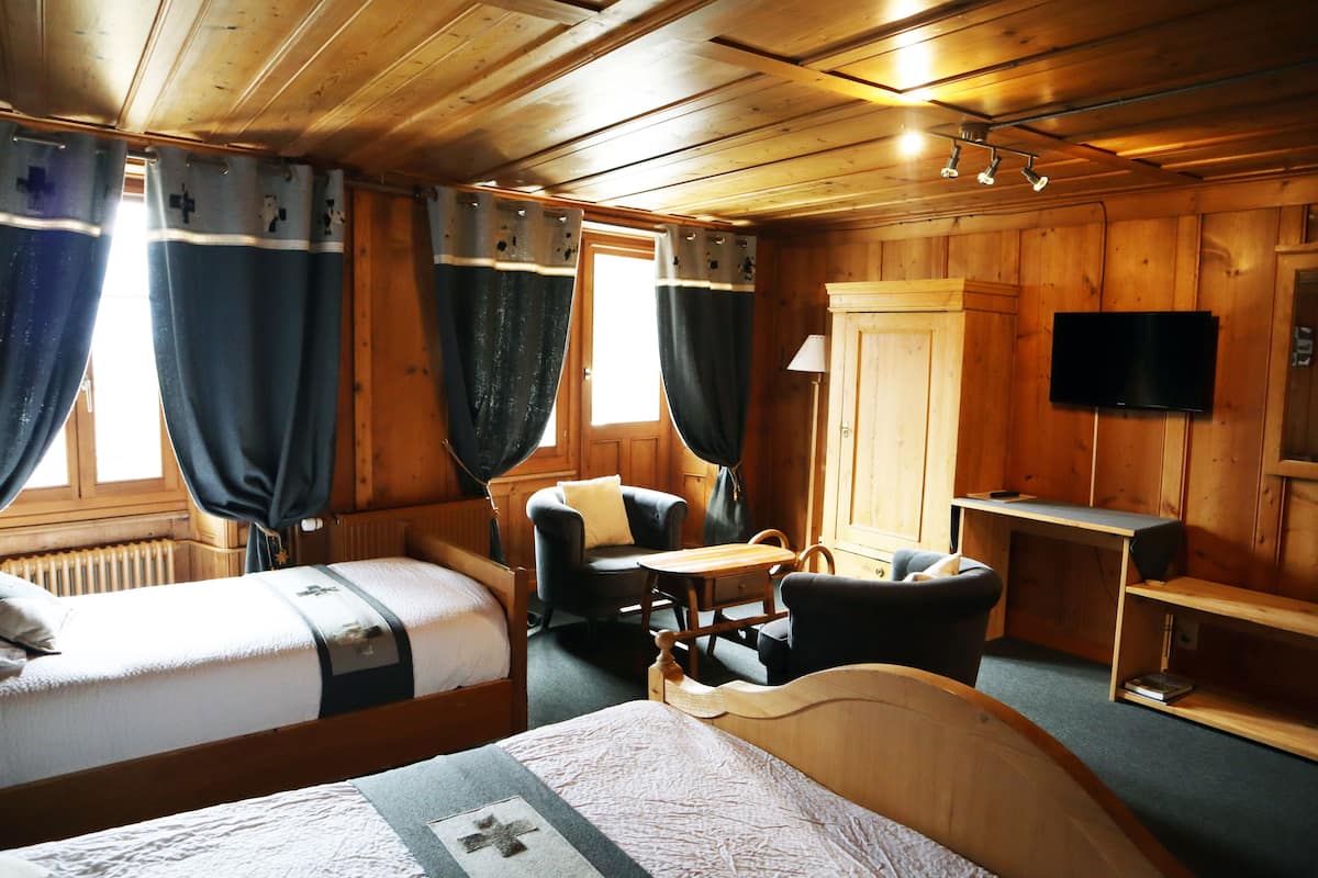 A wooden cabin room with two beds, a desk, a chair, and a television.