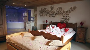 A bedroom with a large bed, a wooden headboard, a wall-mounted artwork, a nightstand, and a bathroom with a bathtub. - Gruyère-rooms (Gruyeres)