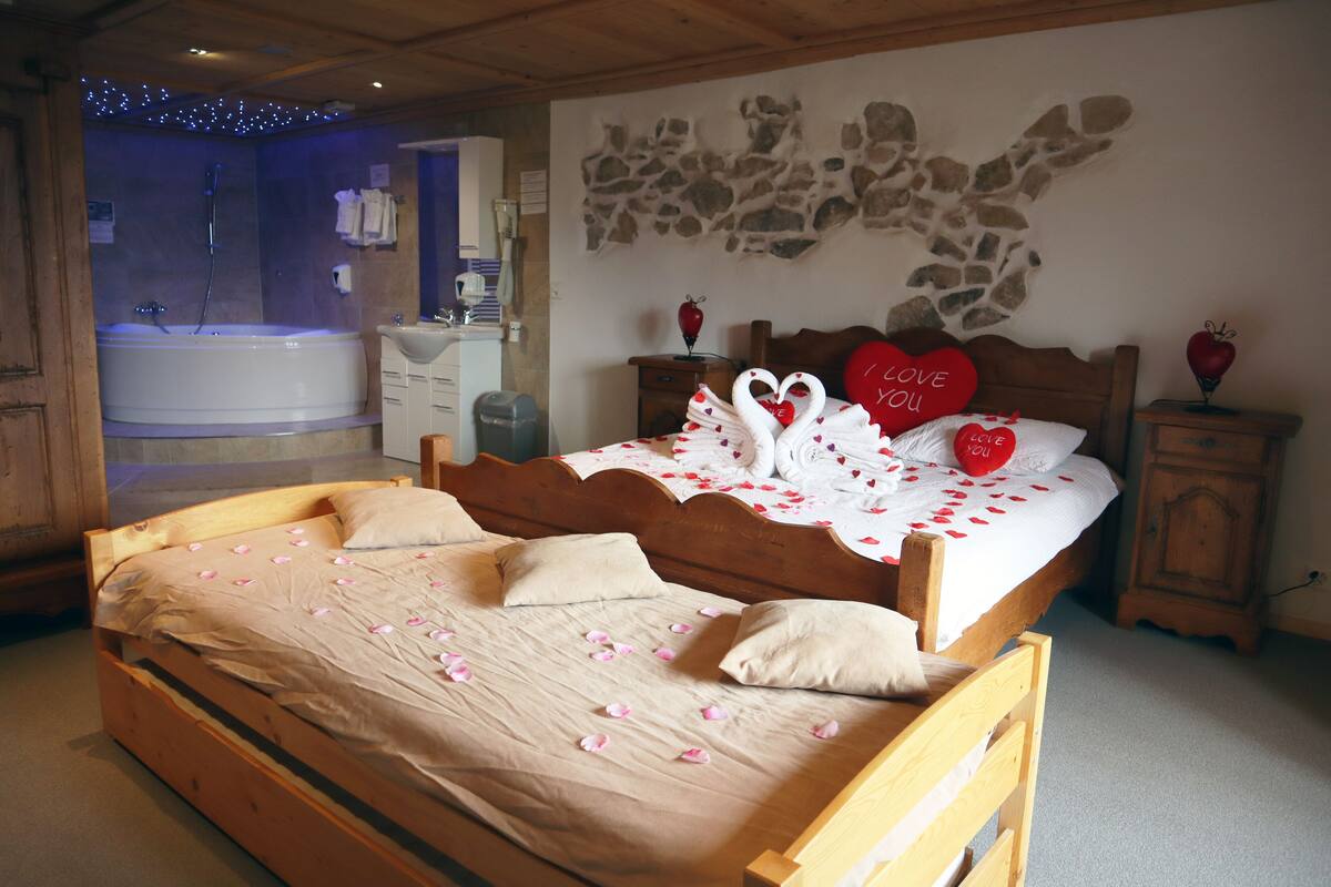 A bedroom with a large bed, a wooden headboard, a wall-mounted artwork, a nightstand, and a bathroom with a bathtub.