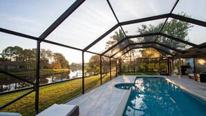 An indoor swimming pool with a glass enclosure, surrounded by a lawn and trees, and a view of a body of water outside.