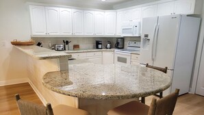 A kitchen with white cabinets, a granite countertop, a built-in microwave, and a refrigerator.