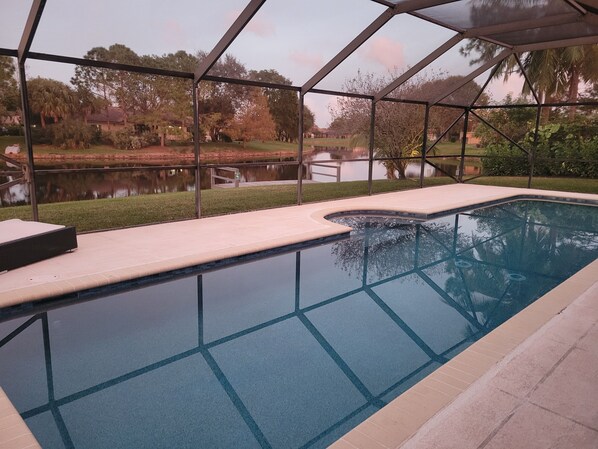 A swimming pool with a clear view of the surrounding landscape, including a body of water and trees. - Golf cart distance to WEF! Charming 3 bedroom waterfront home with heated pool. (Wellington)