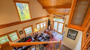 A spacious loft-style living area with a high ceiling, large windows, and a cozy seating area with a sofa and table. - Tranquil 3BR Home; Access To Trails & Mtn. Views! (Breckenridge)