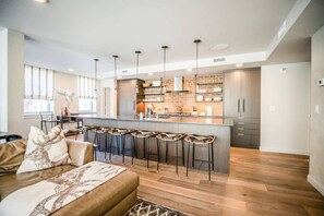 A modern kitchen with a central island, bar stools, and a dining area with a sofa.