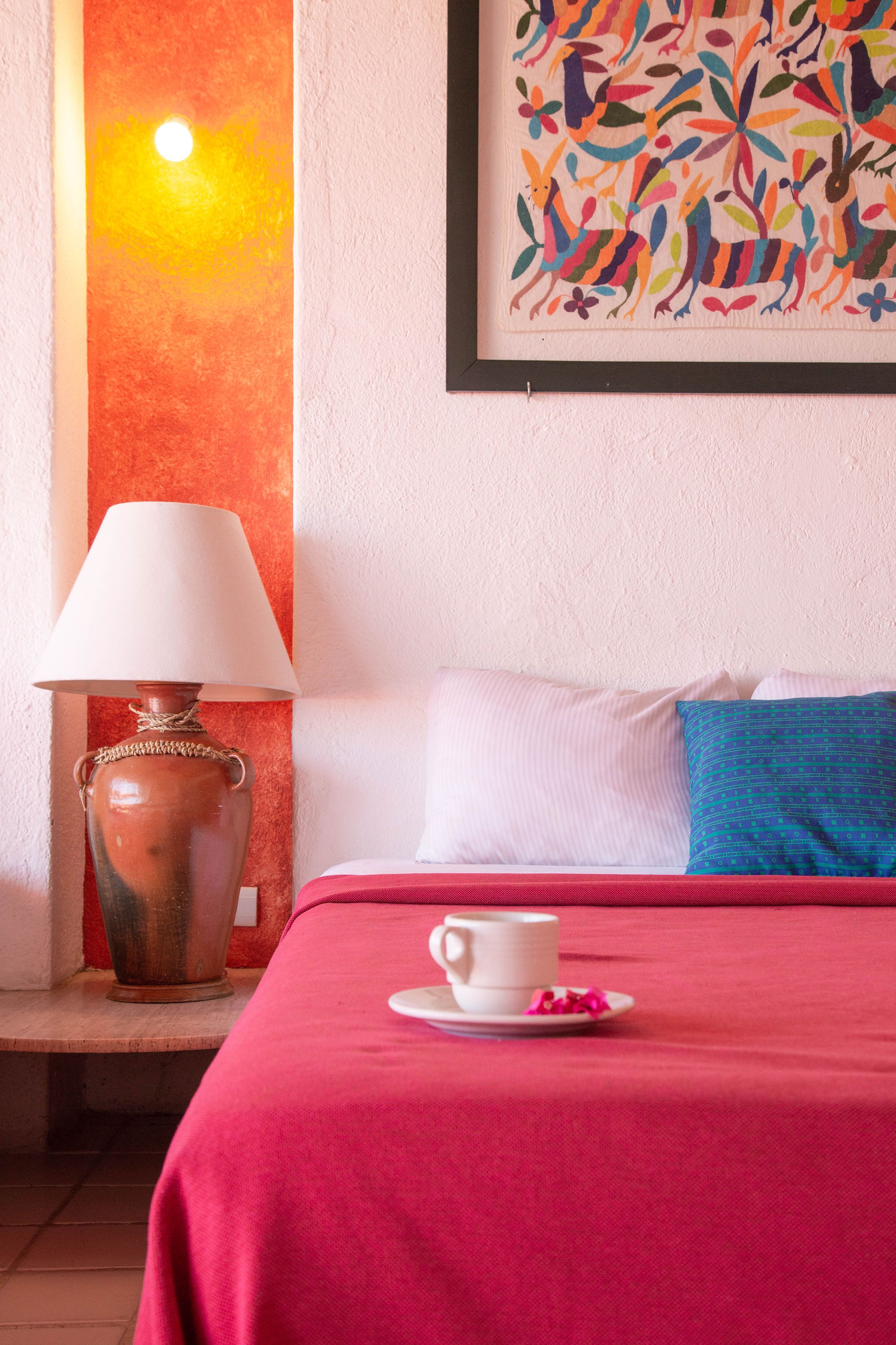 Een hotelkamer met een bed, een lamp, een schilderij en een kopje op het nachtkastje.