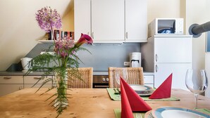 A dining area with a wooden table, a vase with flowers, and a kitchen in the background. - Quiet 55 m² apartment, 3 pers., parking lot, bicycle shed, stove, WLAN (Prerow)