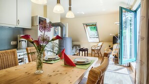 A modern kitchen with a dining area, featuring a wooden table, wicker chairs, and a vase with flowers. - Quiet 55 m² apartment, 3 pers., parking lot, bicycle shed, stove, WLAN (Prerow)