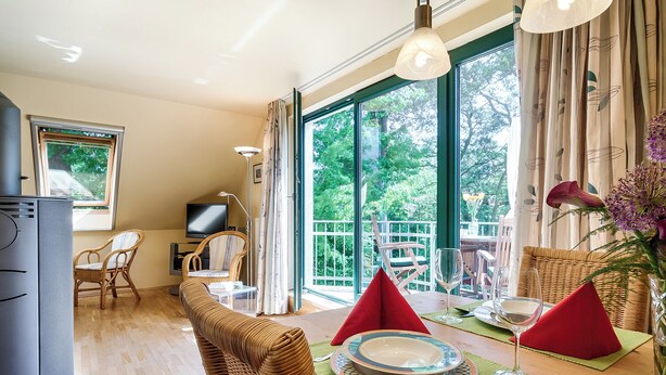 A dining area with a table set for two, a television, and a view of greenery outside. - Quiet 55 m² apartment, 3 pers., parking lot, bicycle shed, stove, WLAN (Prerow)