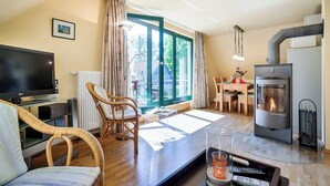 A modern living room with a flat-screen TV, wicker furniture, a glass coffee table, a fireplace, and a dining area with a table and chairs. - Quiet 55 m² apartment, 3 pers., parking lot, bicycle shed, stove, WLAN (Prerow)