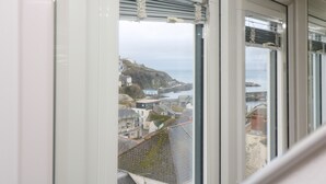 Vista a través de una ventana que muestra un paisaje costero, con edificios y un acantilado.
