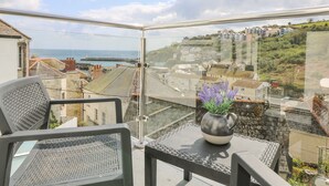 Un balcón con vistas a un pueblo costero, una silla y un florero con flores.