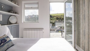 Un dormitorio con cama, radiador, ventana con persianas, estante con adornos y vistas al exterior.
