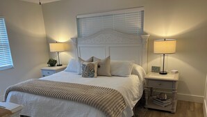 Un dormitorio ordenado con una cama grande, dos mesitas de noche con lámparas, un cabecero decorativo y una alfombra estampada.