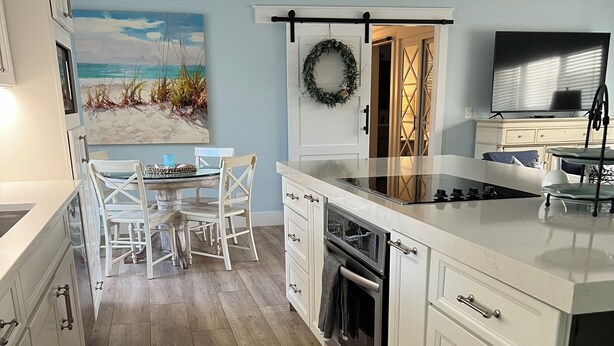 Una cocina moderna con armarios blancos, una isla grande, una zona de comedor con un mural de temática marina y un televisor.