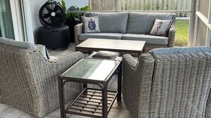 Un espacio de estar exterior con mimbre, que incluye un sofá, dos sillones y una mesa de centro.