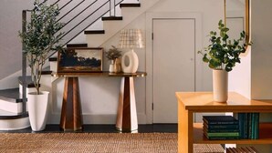 A modern interior with a staircase, a wooden console table with books, a large mirror, and potted plants.