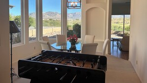 A room with a foosball table, large windows, a chandelier, and a view of mountains. - Resort Golf Course Living With Amazing Golf and Mountain Views (Tucson)