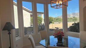 A dining area with a glass table and chairs, a chandelier, and large windows offering a view of a mountainous landscape. - Resort Golf Course Living With Amazing Golf and Mountain Views (Tucson)