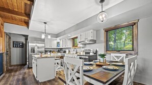 A modern kitchen with white cabinets, a wooden island, and a dining area with white chairs. - THE Smoky Mountain Views, Comfort, Style, Games  (Gatlinburg)