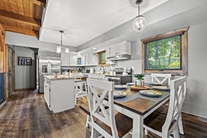 Une cuisine moderne avec des meubles blancs, un îlot central en bois et un coin repas avec des chaises blanches.