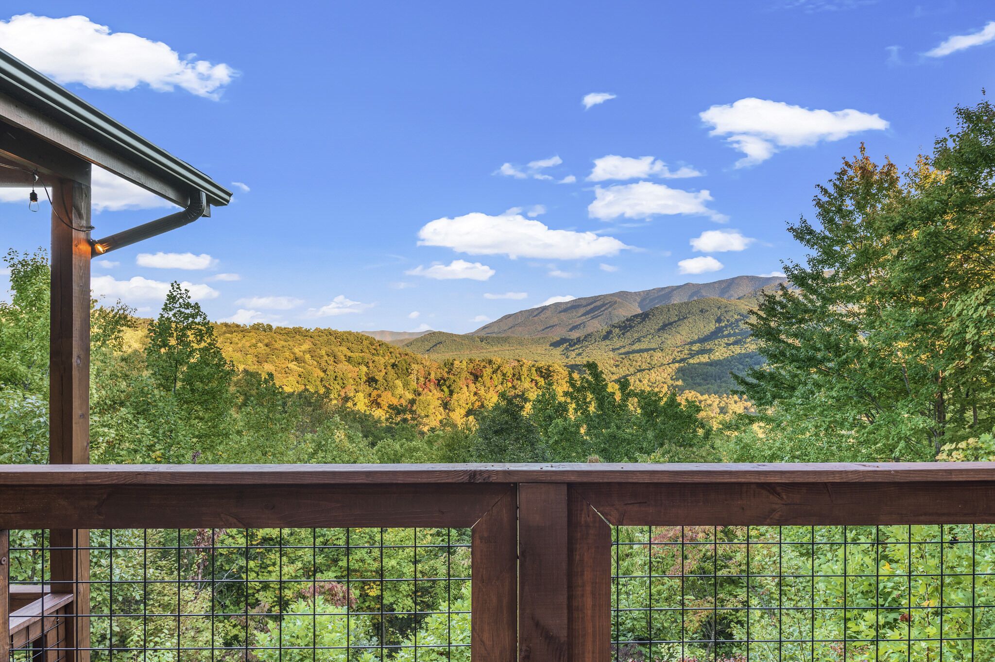 A wooden deck with a metal railing overlooking a mountainous landscape with trees and a clear sky.