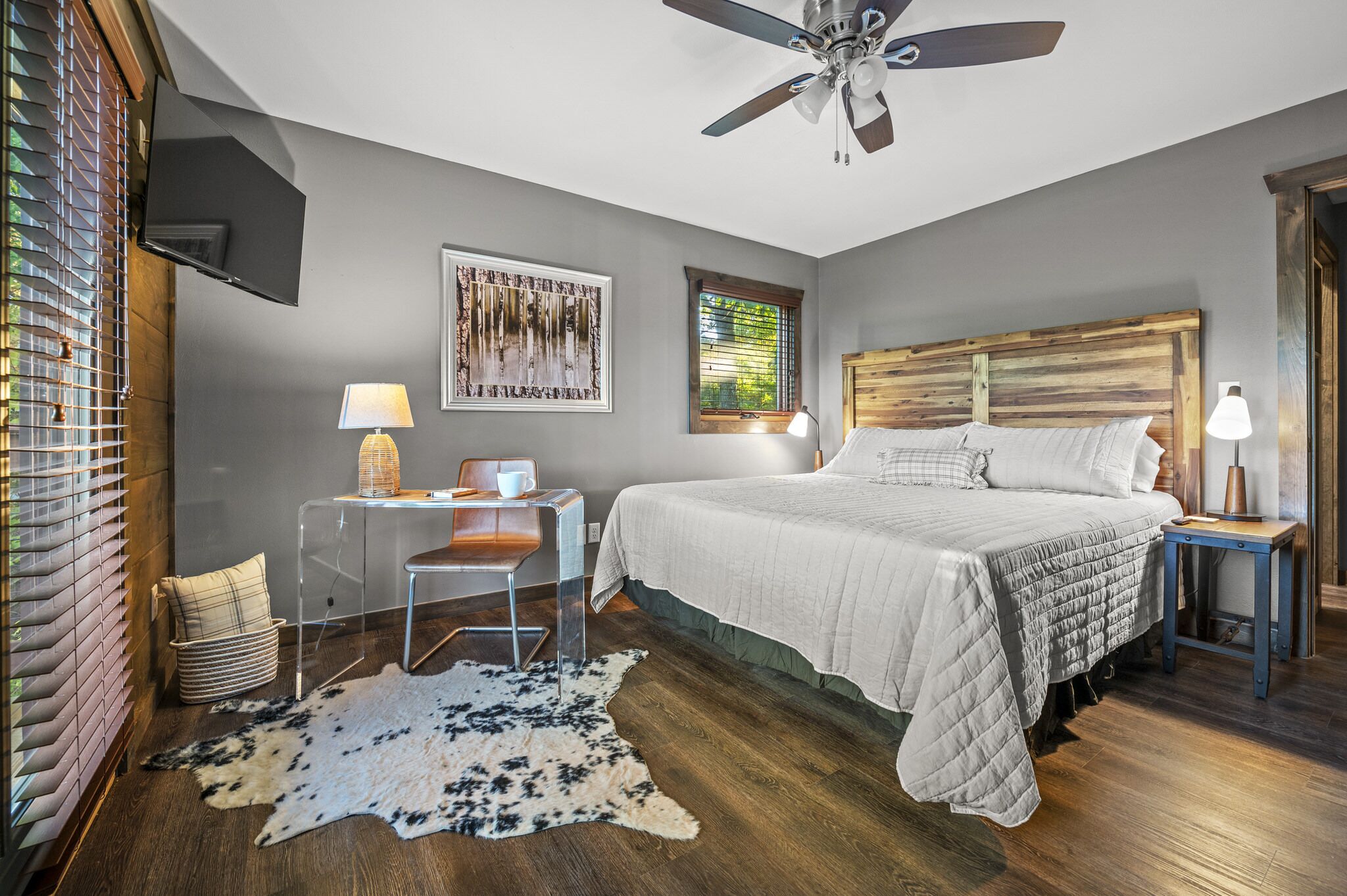 A bedroom with a bed, a desk, a chair, a ceiling fan, and a window with blinds.