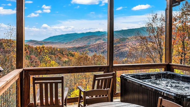 A wooden deck with a hot tub and chairs overlooking a mountainous landscape with autumn foliage. - THE Smoky Mountain Views, Comfort, Style, Games  (Gatlinburg)