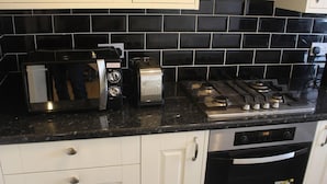 Une cuisine avec un dosseret de carrelage noir, une cuisinière, un four à micro-ondes et des meubles de cuisine blancs.