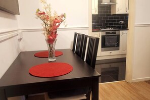 Enjoy meals in this dining area with a table for two, a vase with flowers, and a modern kitchen nearby.
