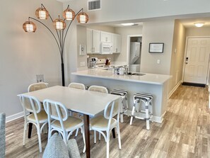 A modern kitchen with white cabinetry, a central island, and a dining area with white chairs and a table. - Pet Friendly • Pool + Beach • Sleeps 8 (Mexico Beach)